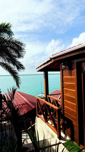 A wooden structure with a red roof overlooking a body of water, with a palm tree in the foreground. - Hotel Maria Isabel Bacalar (Bacalar)