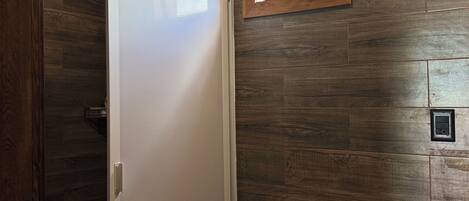 A bathroom with a wooden wall, a white toilet, and a window with a view of greenery.