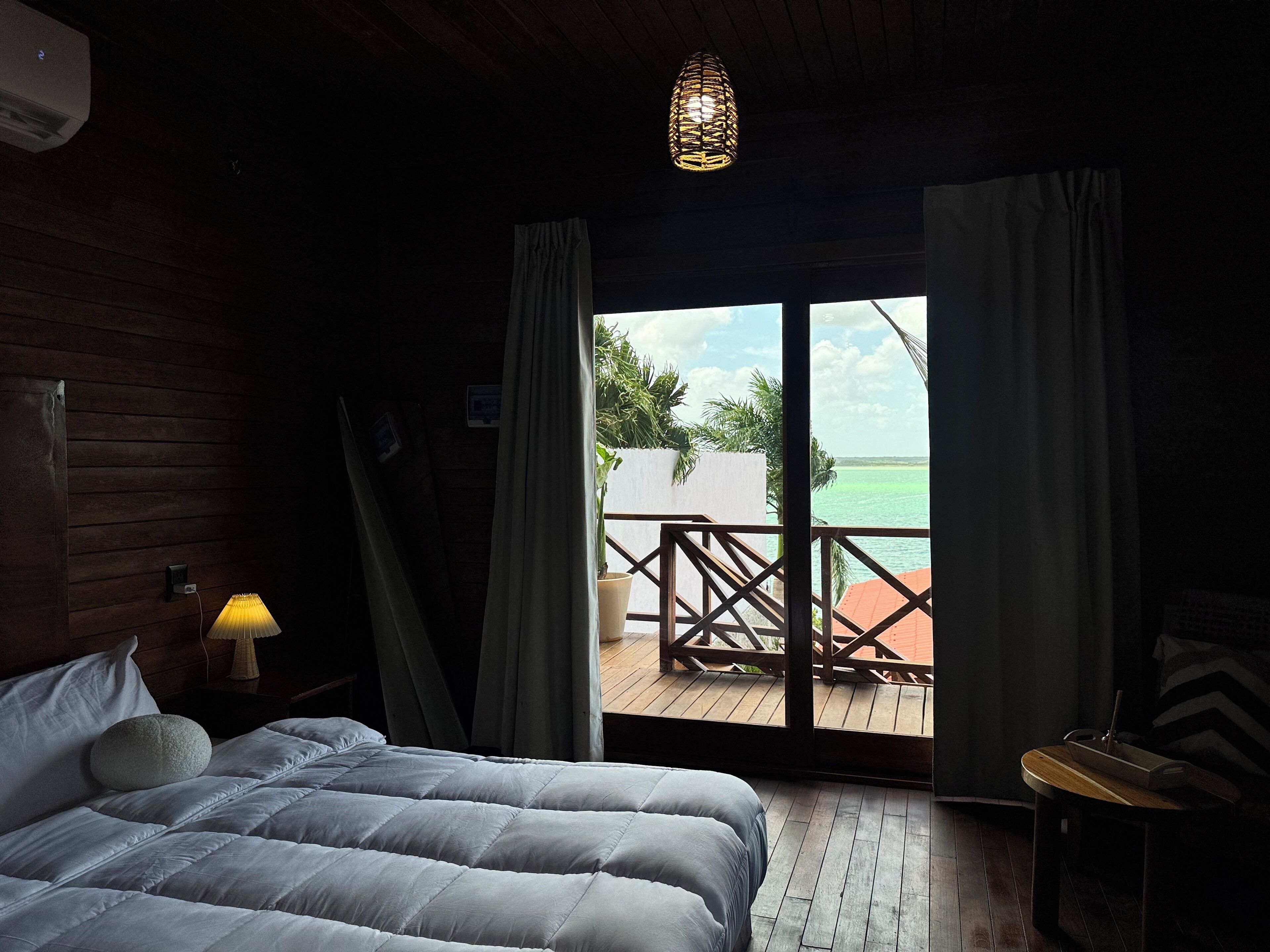 Un dormitorio con una cama, una mesita de noche con lámpara, una ventana con cortinas y vista al océano.