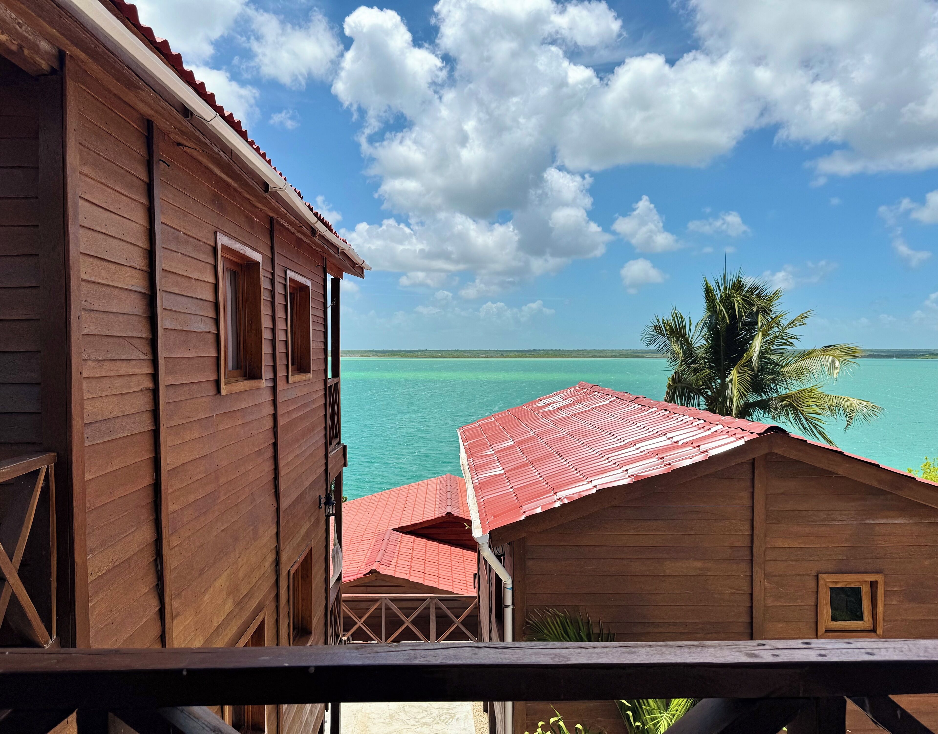 A wooden building with a red roof overlooking turquoise water and a clear sky.