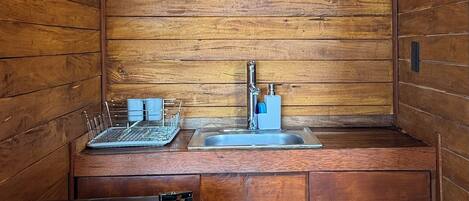 Una cocina compacta con paredes de madera, una lámpara colgante, un lavamanos y un refrigerador.