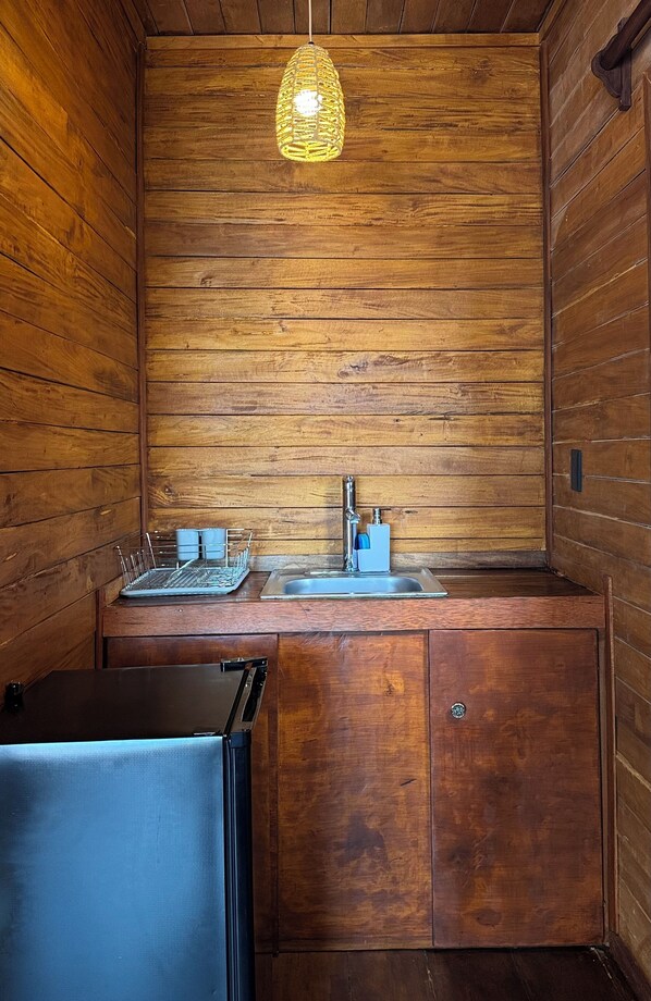 Eine kleine Küche mit Holzwänden, einer Hängeleuchte, einem Spülbecken und einem Kühlschrank.