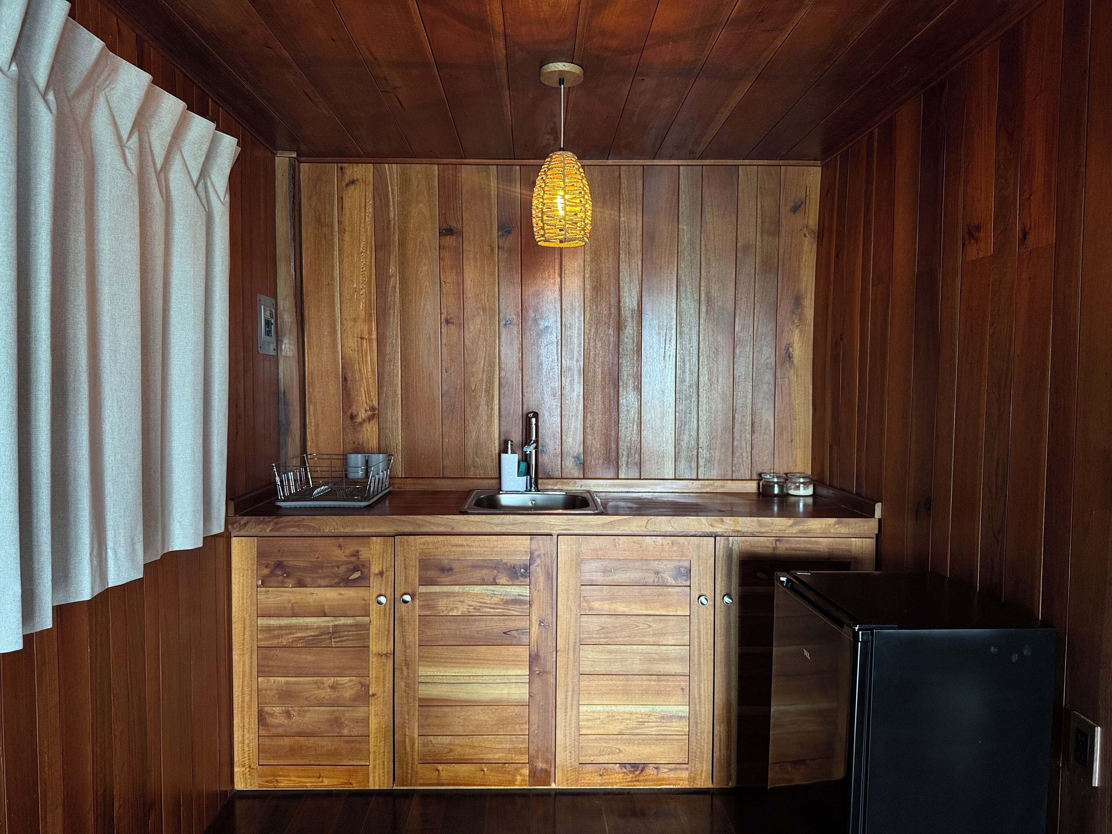 A wooden kitchen with a sink, cabinets, and a refrigerator.