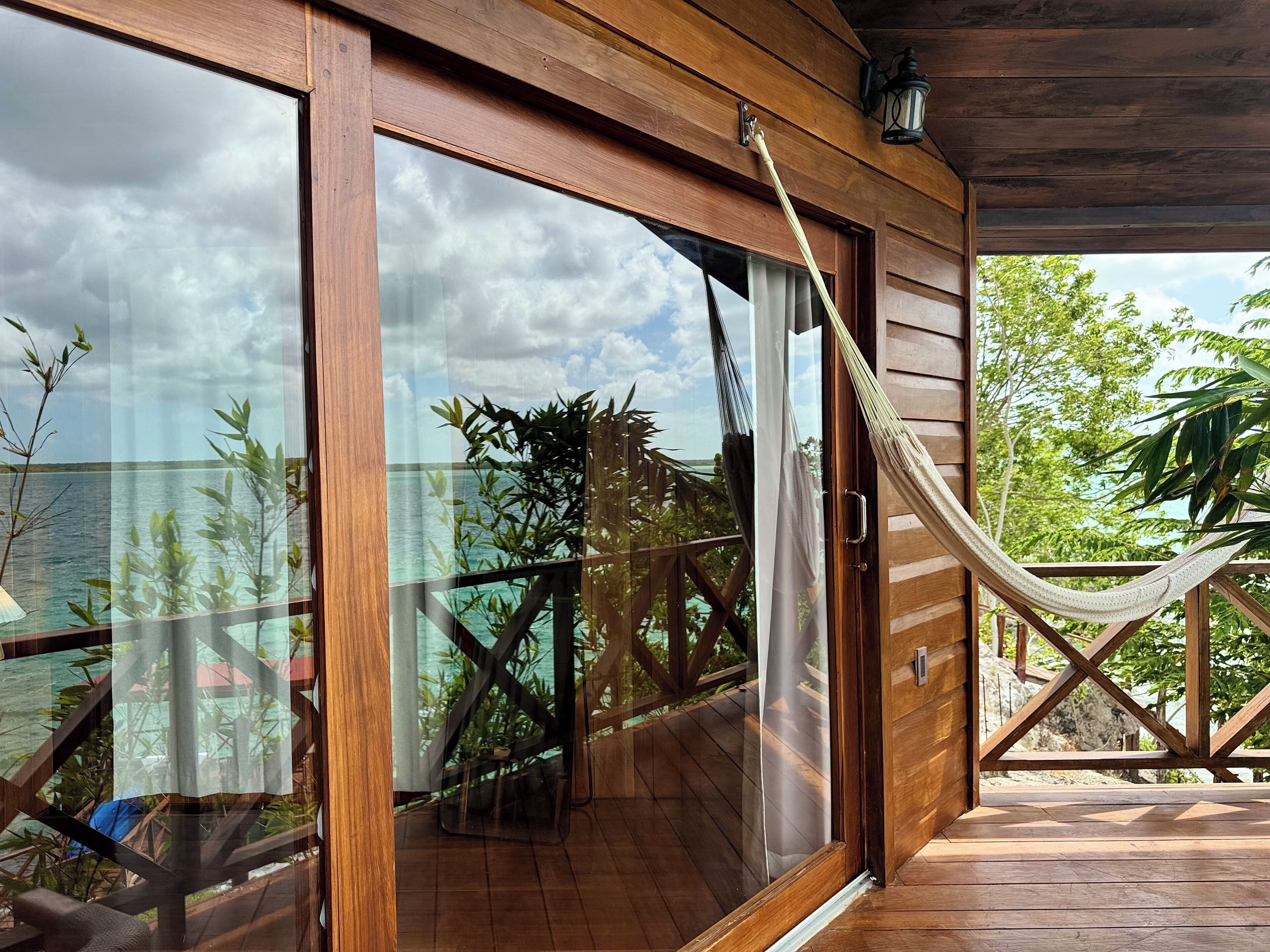 A wooden deck with a glass door leading to a balcony, a hammock, and a view of the sea.