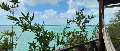 A wooden deck with a hammock, overlooking turquoise waters and a clear sky.