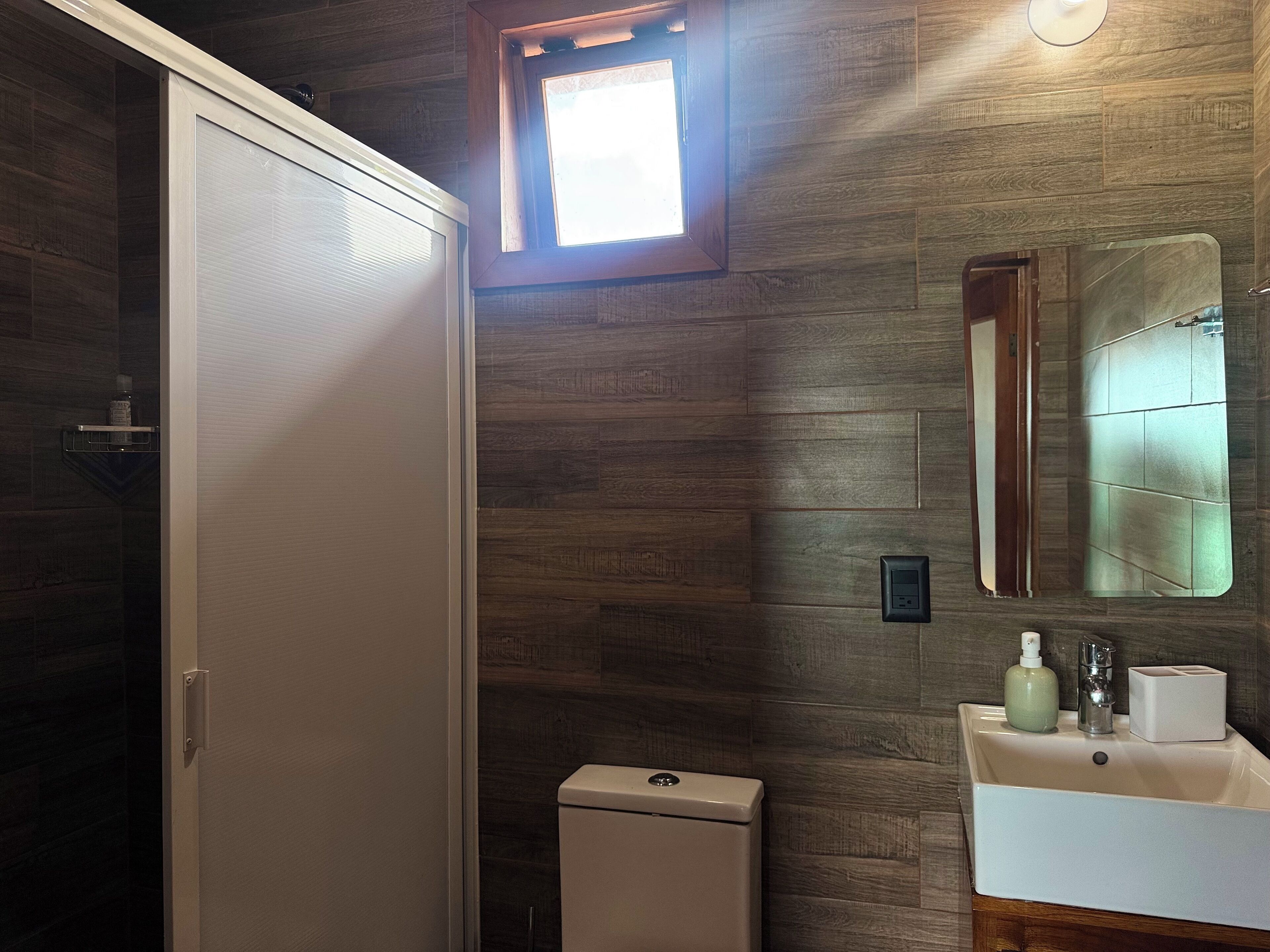 Une salle de bain avec un mur en bois, une fenêtre, des toilettes et un lavabo avec un miroir.
