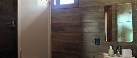 Un baño con pared de madera, una ventana, un inodoro y un lavabo con espejo.