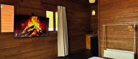 A cozy room with a bed, a TV displaying a fireplace, wooden walls, and a hanging light fixture.