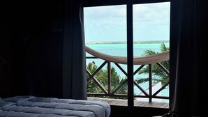 Une chambre avec une grande fenêtre donnant sur une mer turquoise et un hamac.