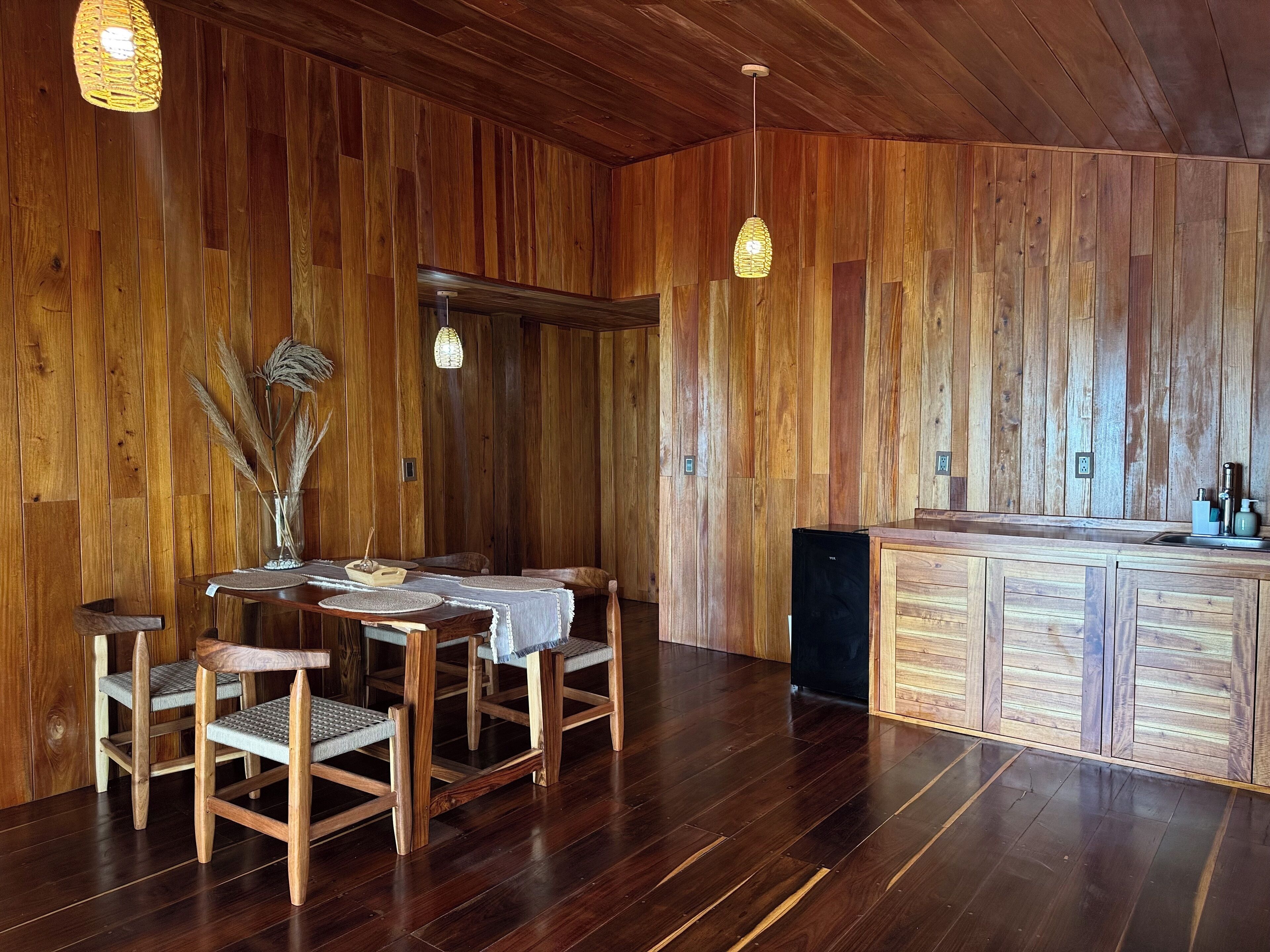 A wooden interior with a dining table, chairs, and a kitchen area.