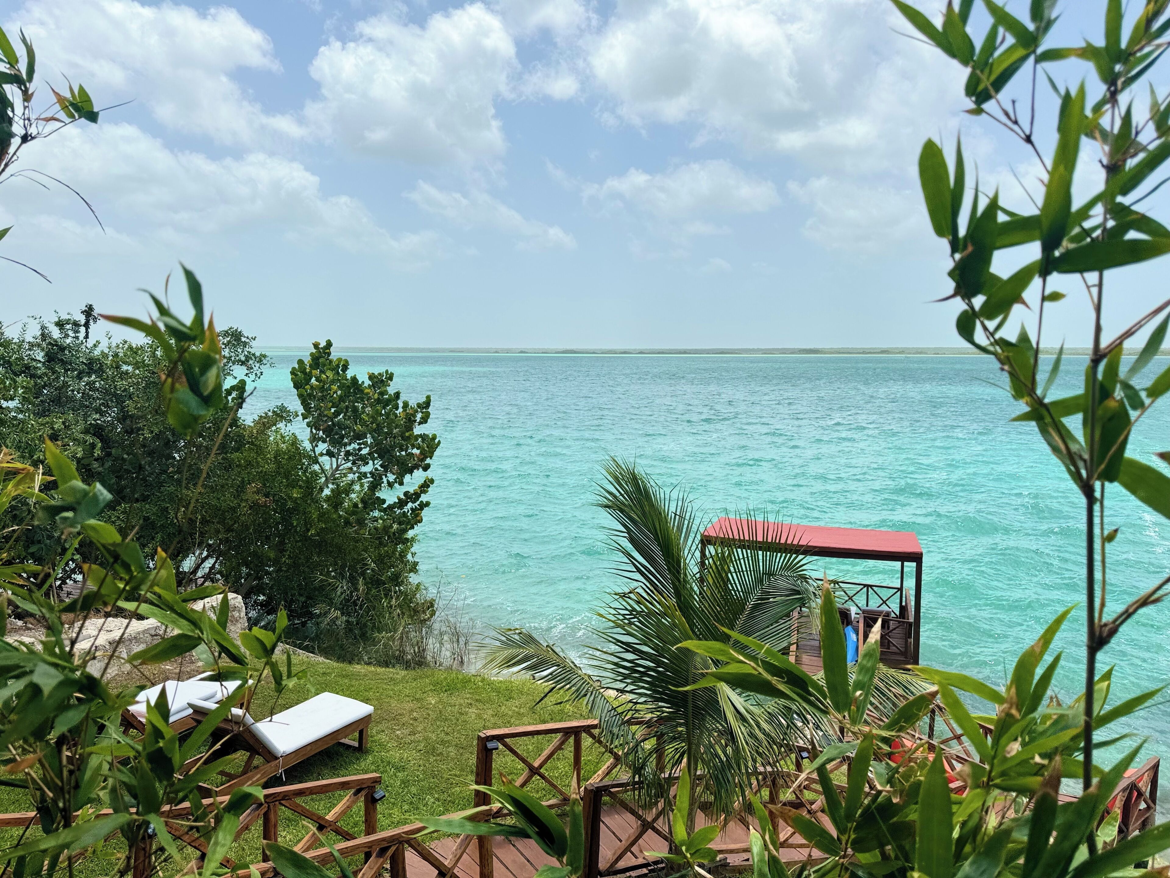 A beach view with lounge chairs and a wooden deck overlooking turquoise waters.