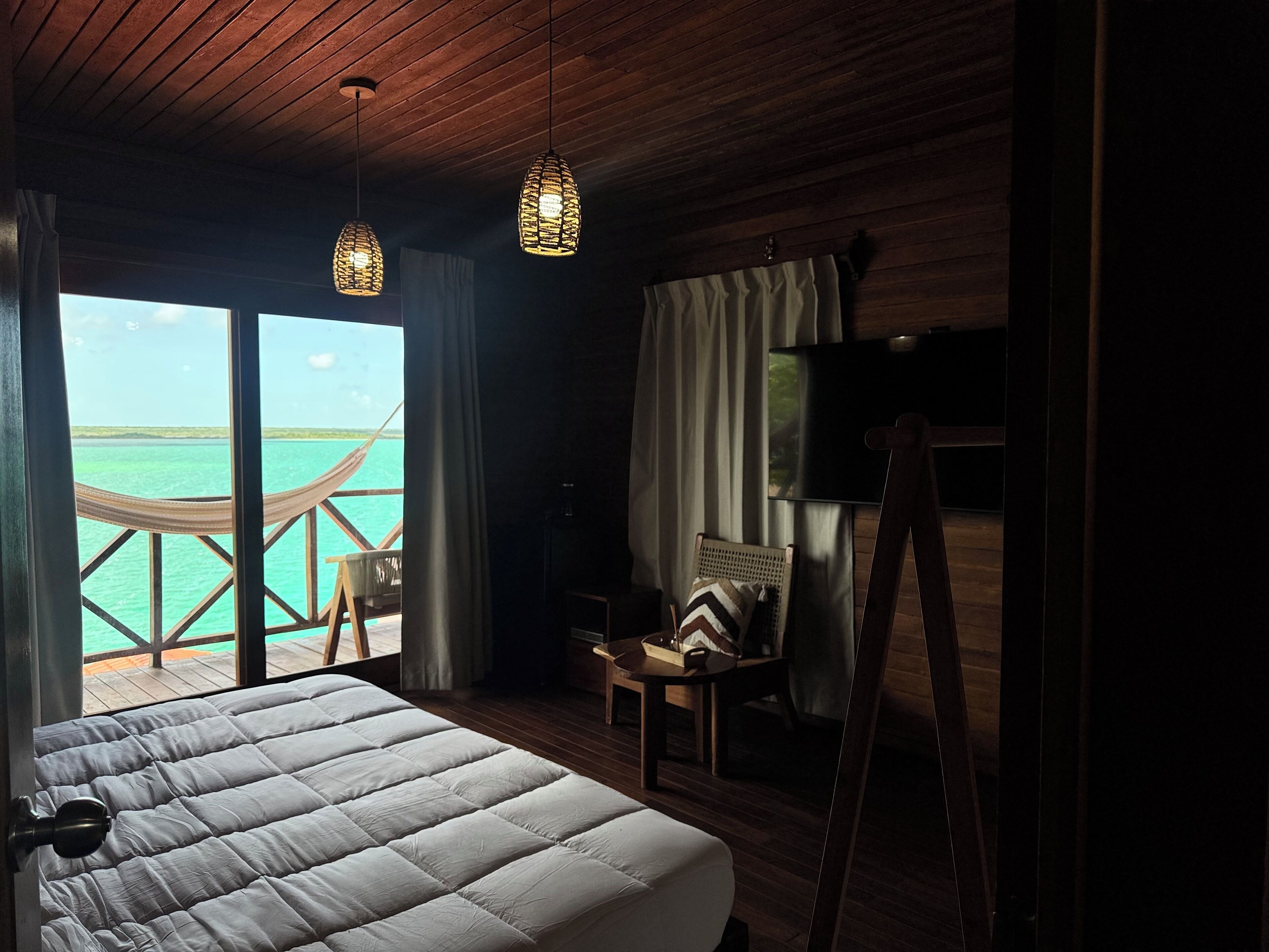 Una camera da letto con un letto grande, soffitto in legno, televisione, una sedia e vista sull'oceano.