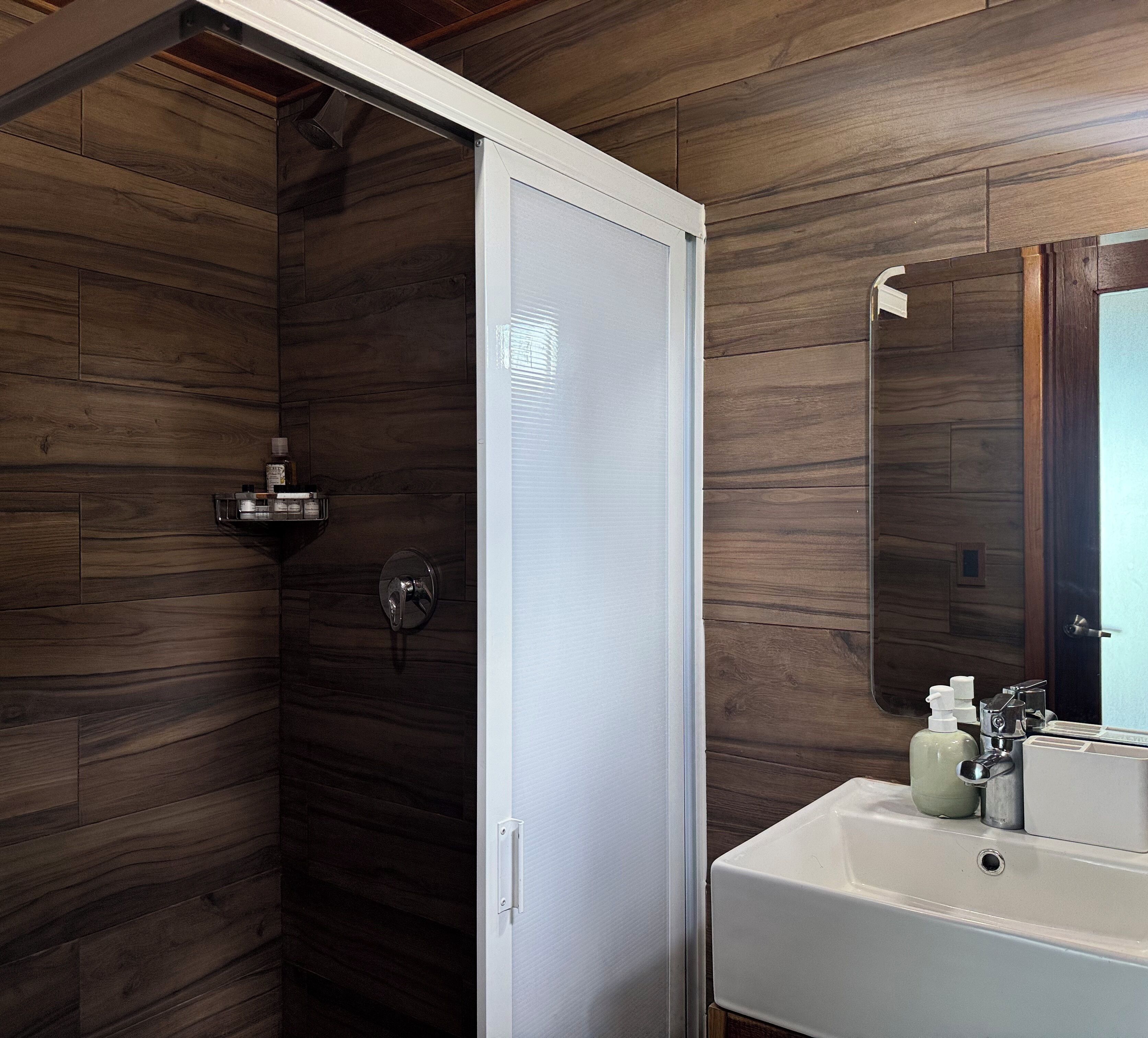 Een moderne badkamer met een ruime douche, een wastafel met toiletartikelen en een spiegel.