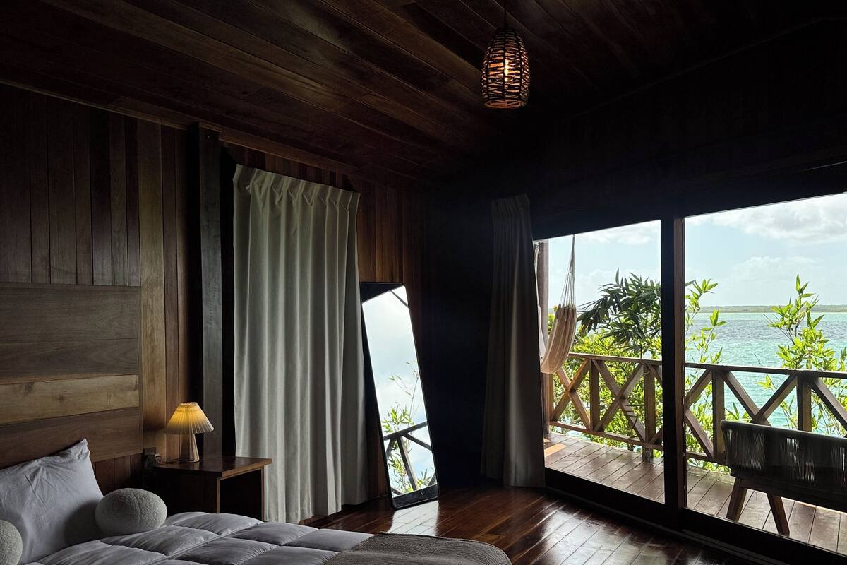 A bedroom with a large bed, wooden ceiling, and a view of the sea through a balcony.