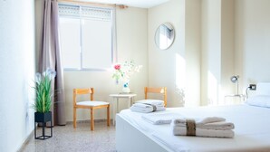 A hotel room with a bed, two chairs, a small table with a vase of flowers, and a window with curtains.