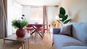 A living room with a sofa, a dining table with chairs, a potted plant, and a window with curtains.