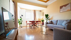A living room with a sofa, a coffee table, and a TV stand. There is a dining area with a table and chairs.