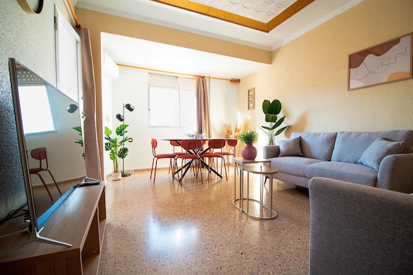 A living room with a sofa, a coffee table, and a TV stand. There is a dining area with a table and chairs.