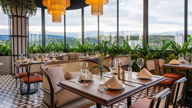 Un restaurant situé sur le toit d’un immeuble, avec des tables dressées pour le dîner, offrant une vue panoramique sur la ville.