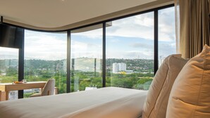 Une chambre d’hôtel avec un grand lit, un bureau et une vue sur le paysage urbain, grâce à de grandes fenêtres.
