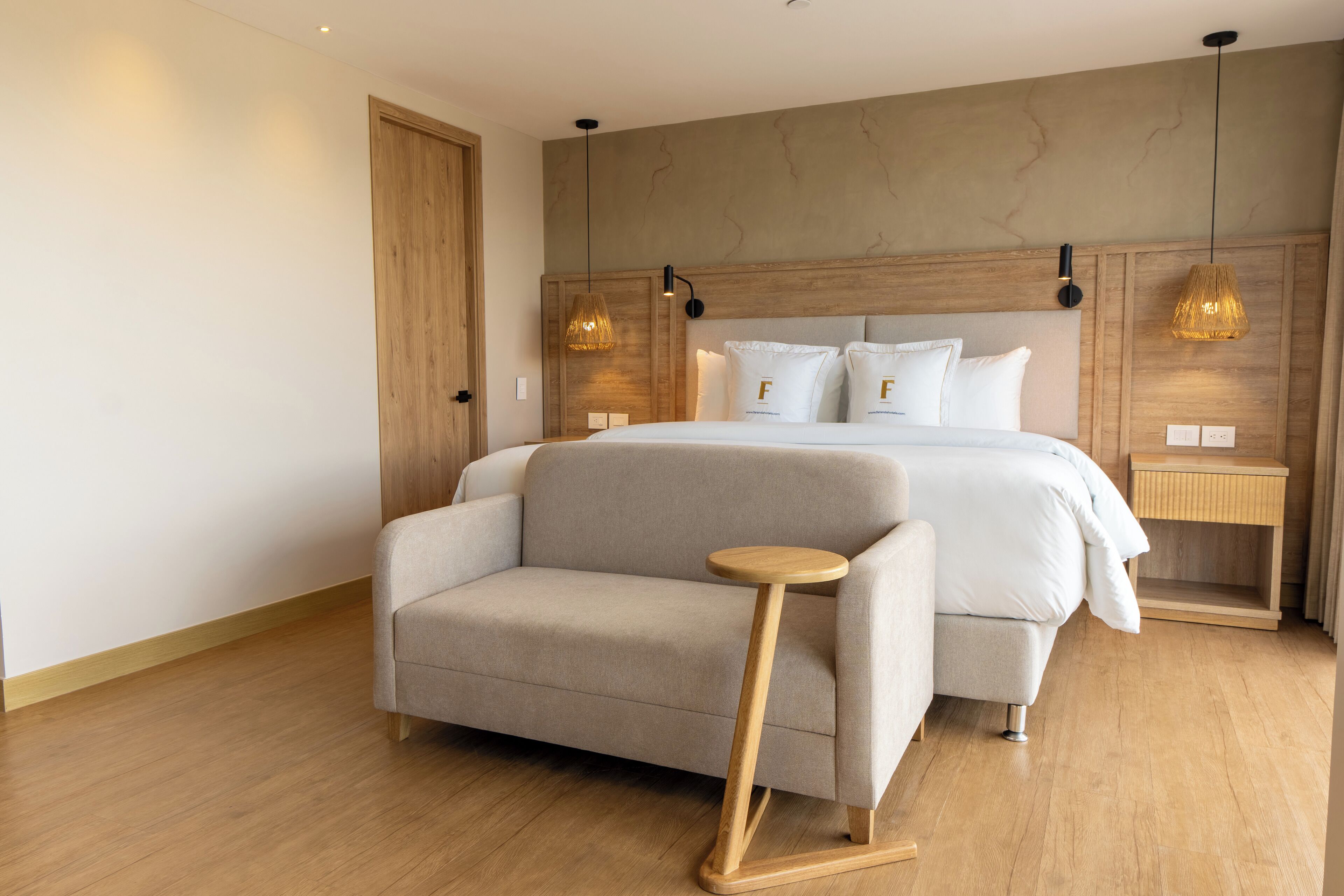 Un dormitorio moderno con una cama, un sofá, una mesita de madera y dos lámparas de noche.
