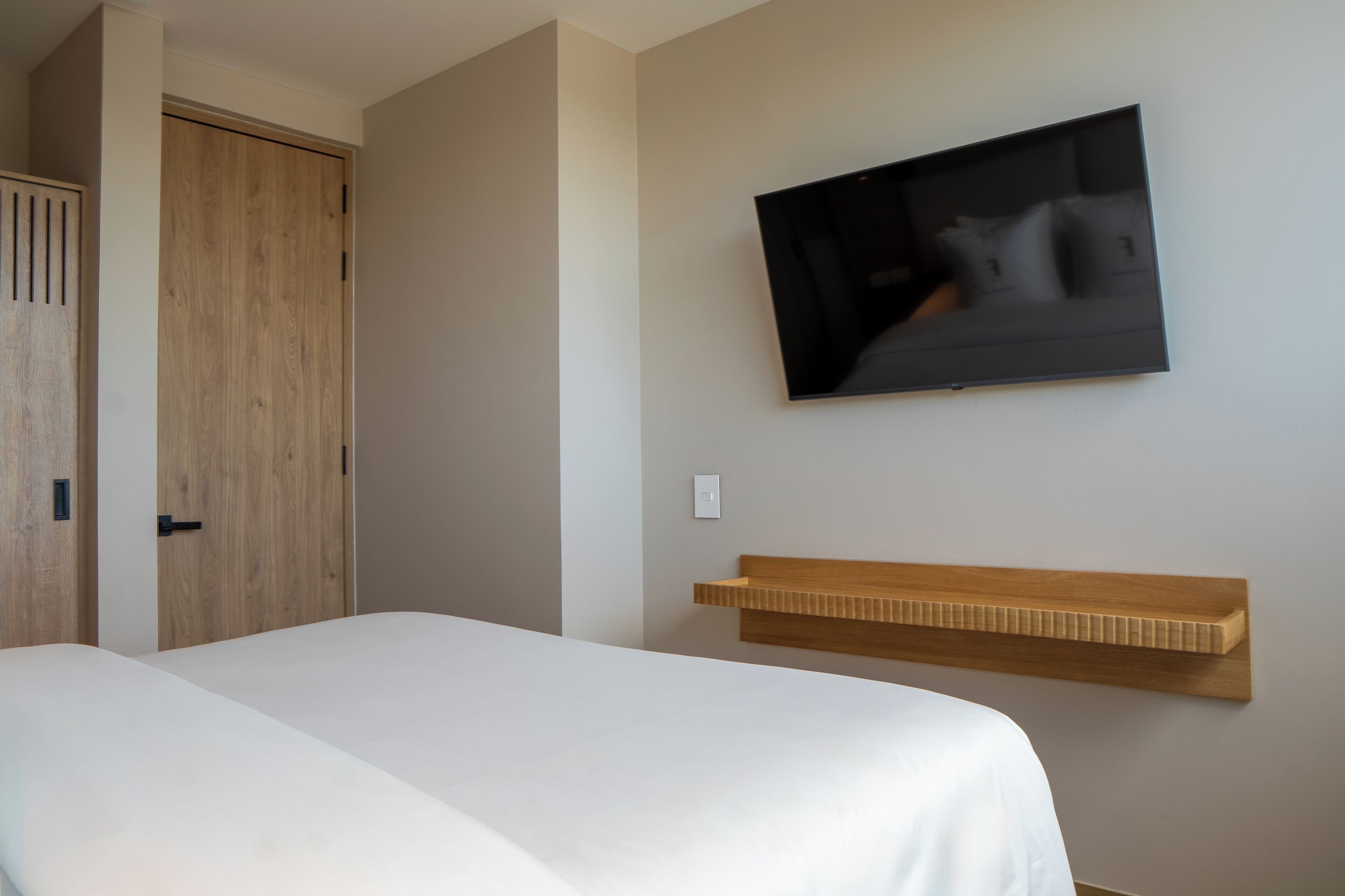 Een slaapkamer met een bed, een houten garderobe, een wandtelevisie en een houten plank.