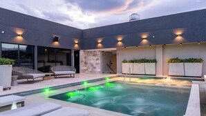 Un espace piscine extérieur moderne, doté de chaises longues, d’un jacuzzi et d’un éclairage d’ambiance.