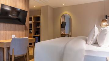 Ein Hotelzimmer mit Bett, Schreibtisch, Stuhl, einem an der Wand befestigten Fernseher und einem Kleiderschrank.