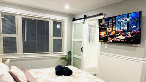 A bedroom with a bed, a TV mounted on the wall, a sliding door, and a window with blinds. - 1-bedroom unit with Private Entrance/ Laundry/Kitchen/Parking (Abington)