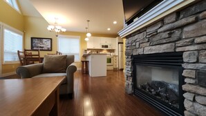 Una cocina moderna con armarios blancos, una chimenea de piedra y un comedor con mesa y sillas de madera.