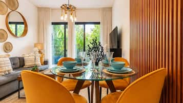 A dining area with a glass table, orange chairs, and a view of greenery outside.
