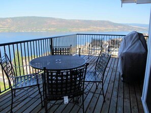 Eine Terrasse mit einem runden Tisch und Stühlen, mit Blick auf ein Gewässer und Hügel.