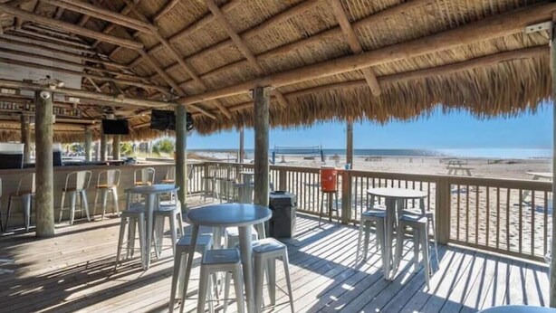 A beachside patio with thatched roof, wooden deck, and outdoor seating. - Modern Serenity - Steps to Beach and Coligny Plaza (Hilton Head Island)