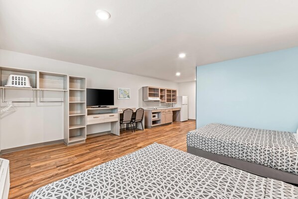 A modern bedroom with a wooden floor, a desk with a chair, a bed with patterned bedding, and built-in shelving. - Woodspring Suites Charlotte - Arrowood (Charlotte)