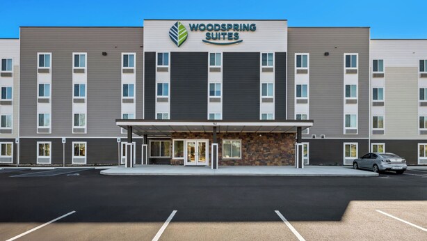 Un hotel con fachada moderna, un logotipo destacado y un estacionamiento al frente.