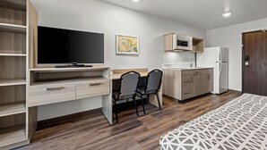 Una habitación compacta con televisor, una mesa de comedor con sillas, microondas, refrigerador y un mueble de madera.