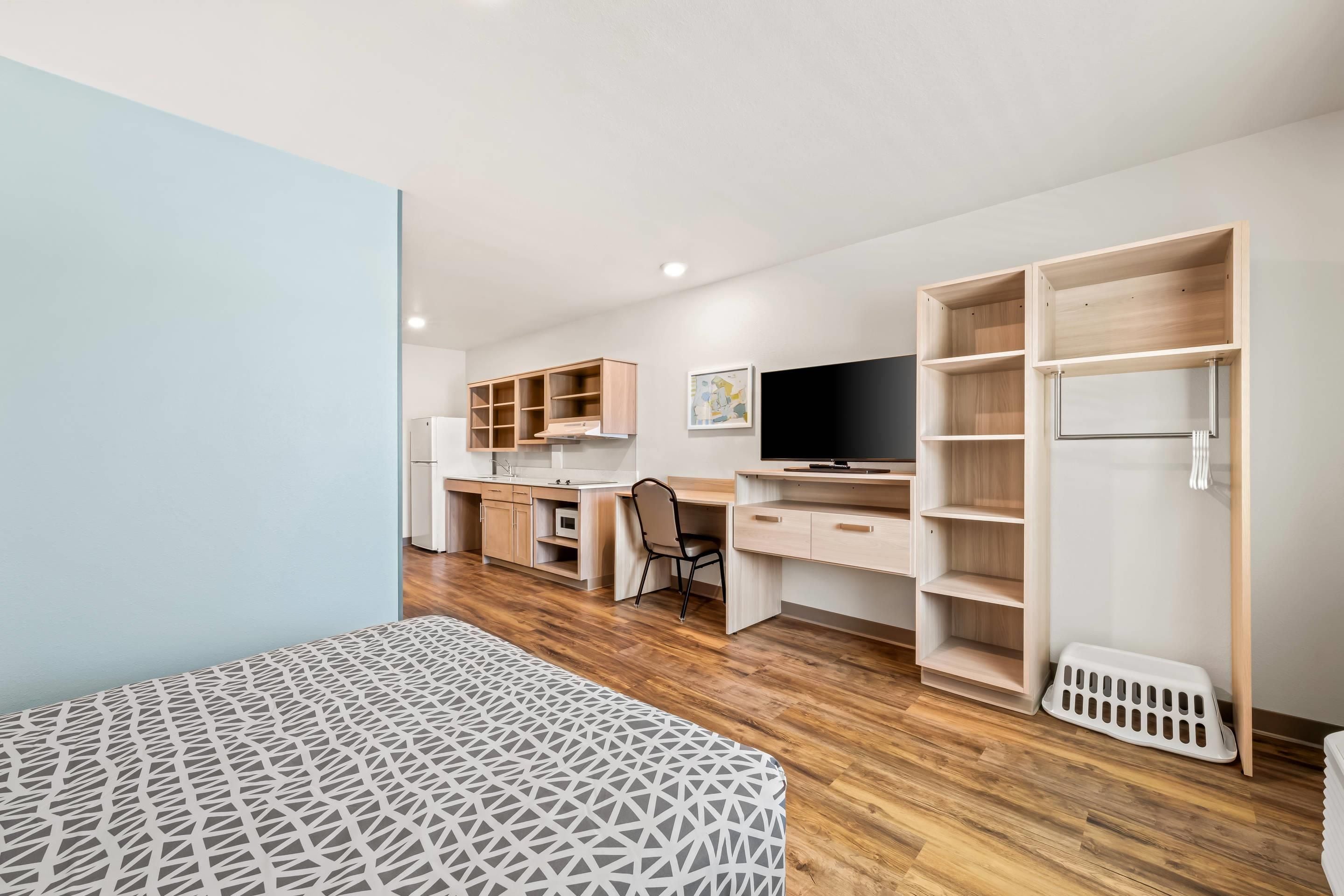 A modern bedroom with a bed, a desk, a TV, and built-in shelving.