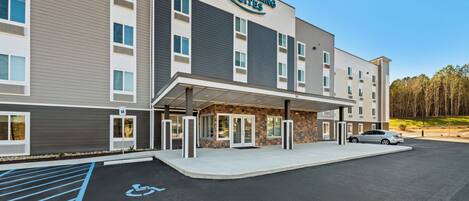 A modern hotel with a covered entrance, a handicap parking space, and a car parked in front.