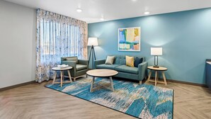 Una sala de estar moderna con una pared azul, un sofá verde, una mesa de centro redonda y dos mesitas de noche con lámparas.
