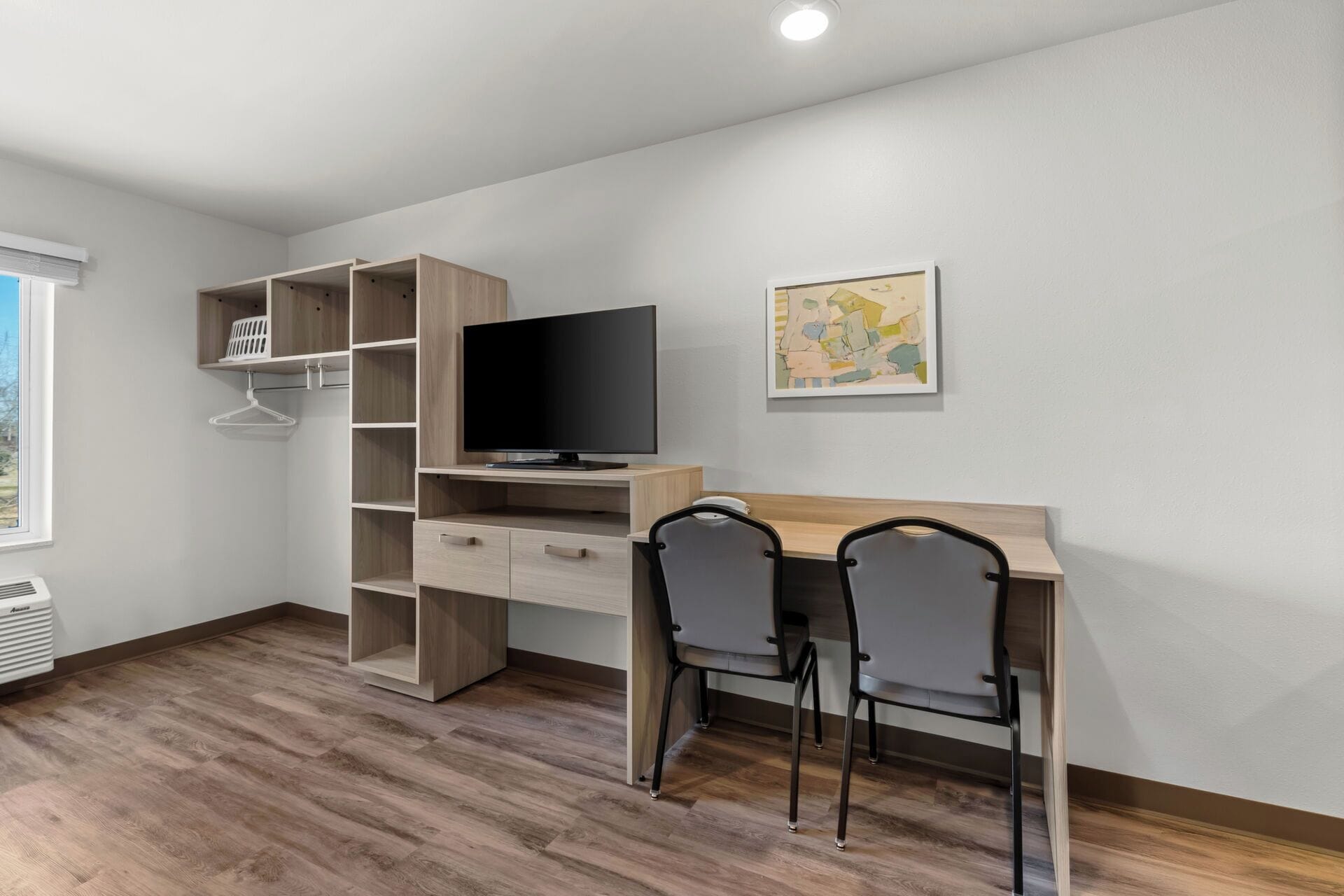 A modern room with a wooden desk, two chairs, a TV, and a shelving unit.