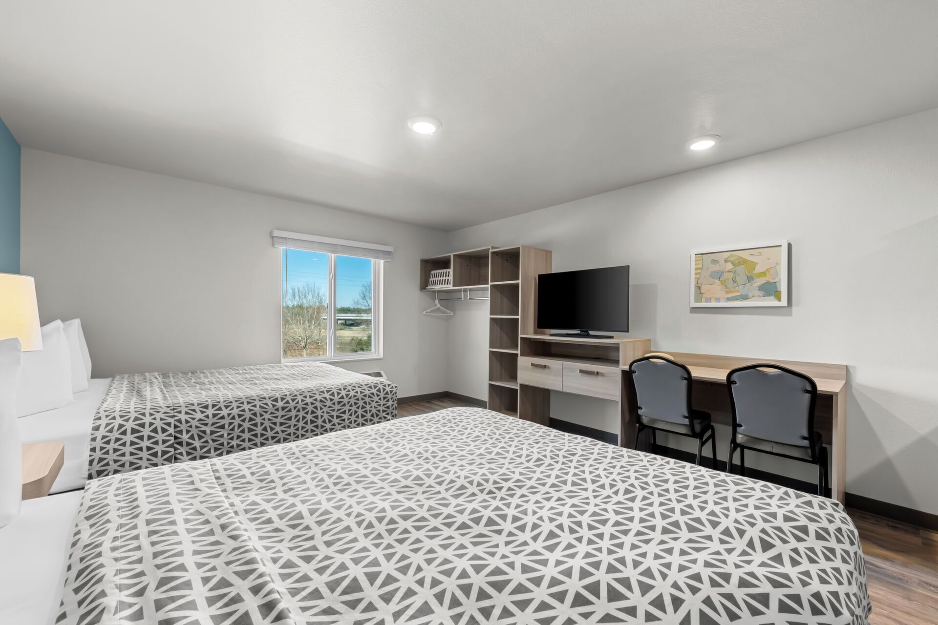 A hotel room with two beds, a TV, a desk with chairs, and a window with a view.
