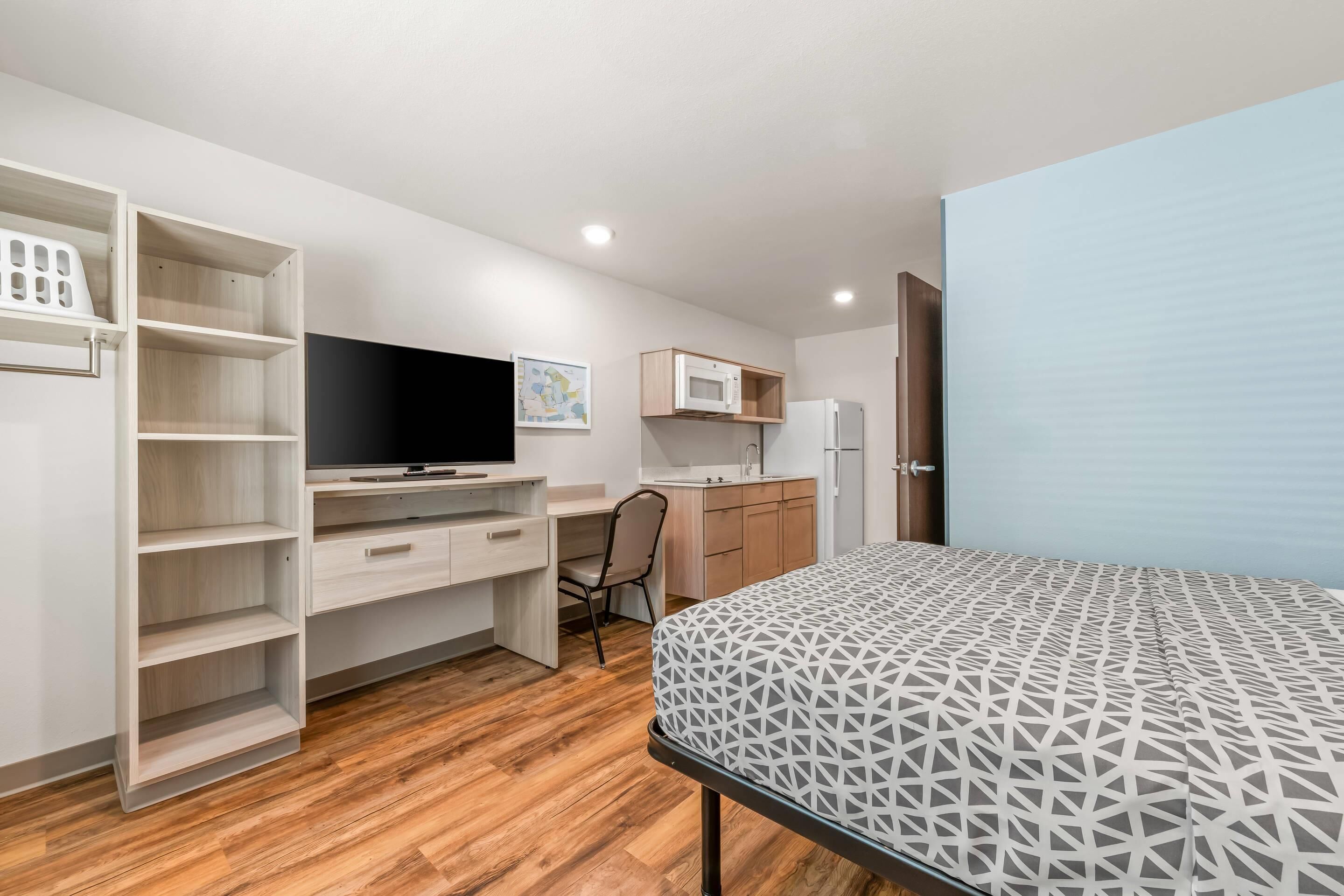 A modern bedroom with a bed, a desk, a chair, a TV, and a wardrobe.