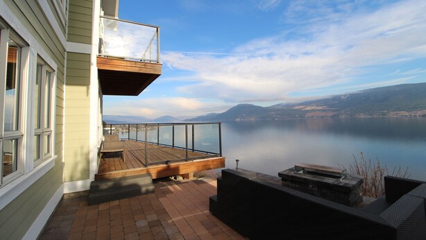 A balcony with a wooden deck, glass railing, and a view of a calm lake and mountains. - Beautiful 3 Bedroom Pet Friendly Cottage on Lake Okanagan (West Kelowna)