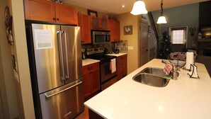 A kitchen with stainless steel appliances, wooden cabinets, and a white countertop. - Beautiful 3 Bedroom Pet Friendly Cottage on Lake Okanagan (West Kelowna)