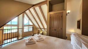 A bedroom with a sloped ceiling, a wooden door, a bed with white linens, and a view through large windows. - Gorgeous Lakeview 2 Bedroom  and  Loft Cottage on Lake Okanagan (Kelowna)