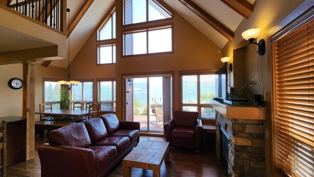 A spacious living area with a leather sofa, a wooden coffee table, and a fireplace. There are multiple windows providing natural light and a view of the outdoors. - Gorgeous Lakeview 2 Bedroom  and  Loft Cottage on Lake Okanagan (Kelowna)