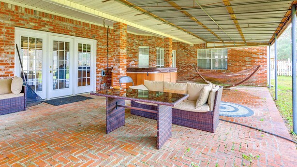 Ein überdachter Patio-Bereich mit Backsteinmauern, einem Glastisch, Korbmöbeln und einer Hängematte.