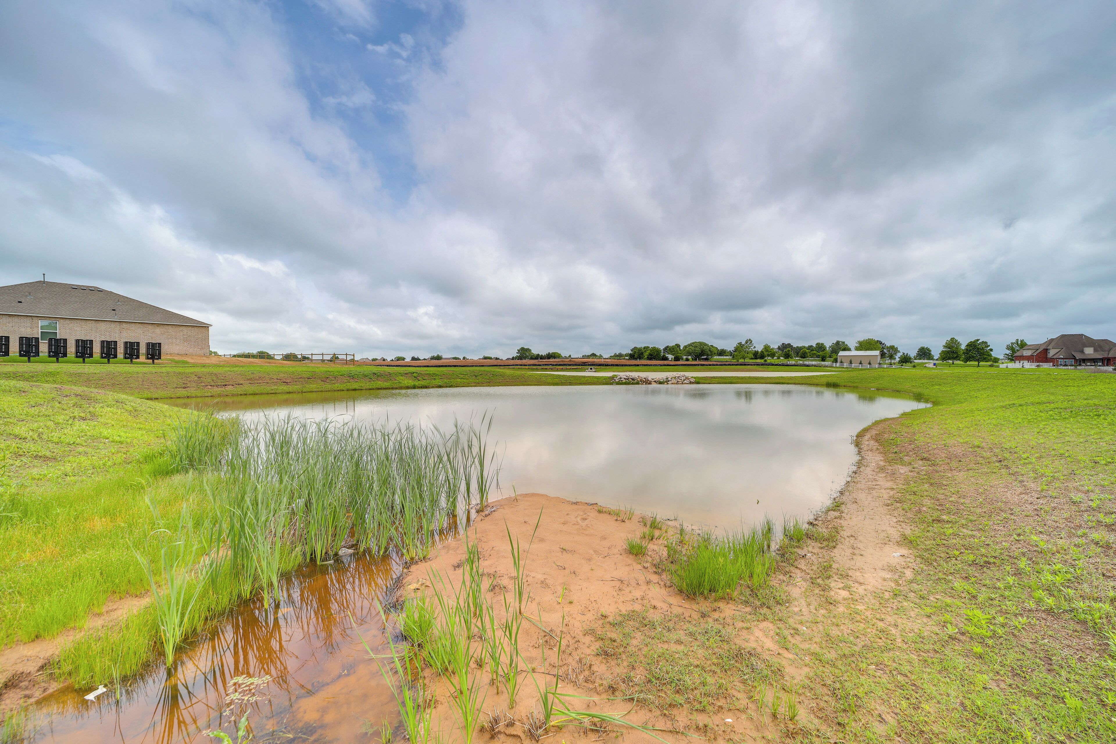 A tranquil outdoor setting with a pond, grassy areas, and a building in the background.