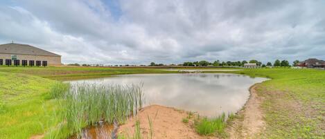 A tranquil outdoor setting with a pond, grassy areas, and a building in the background.