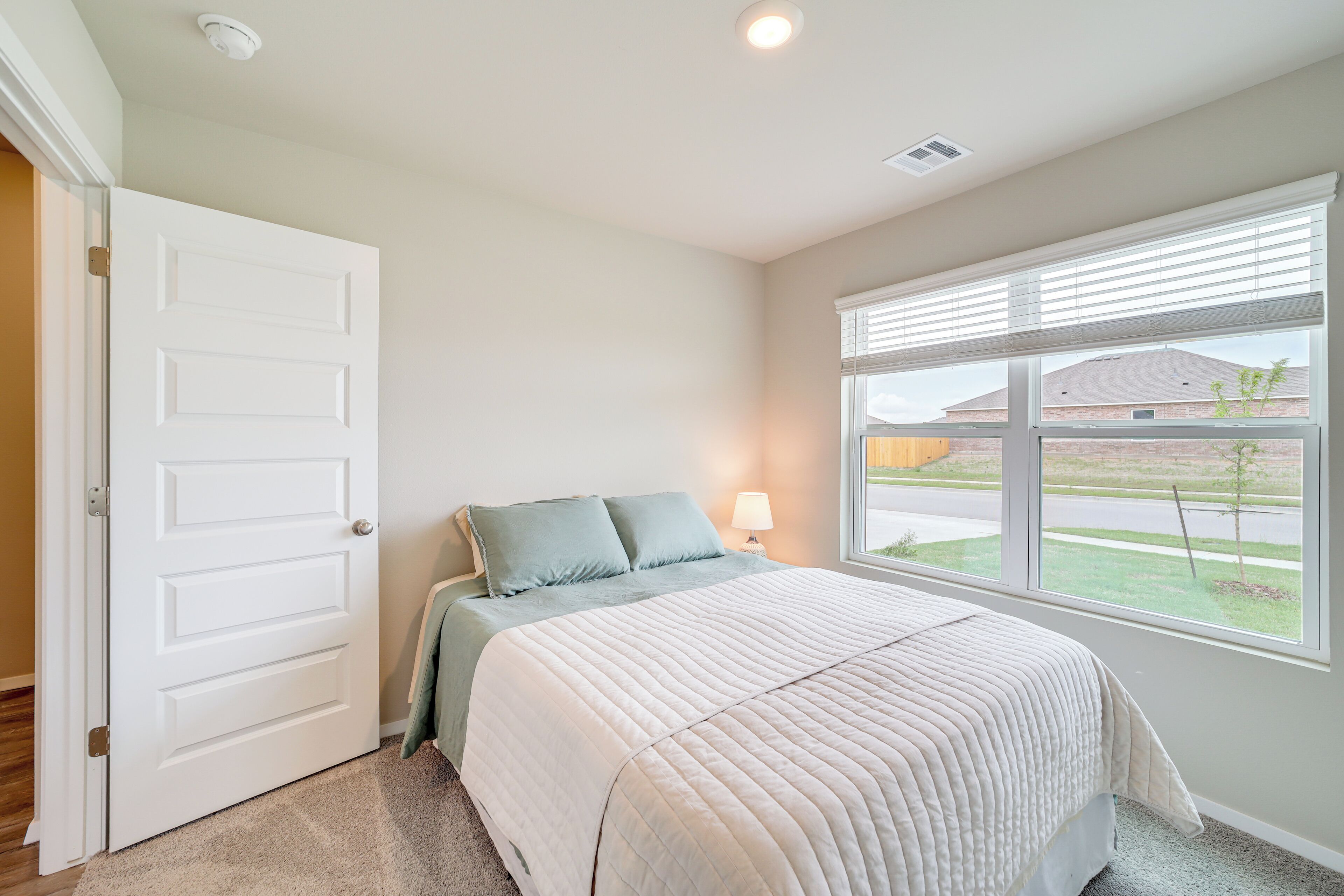 A bedroom with a bed, a window with blinds, a door, and a lamp.